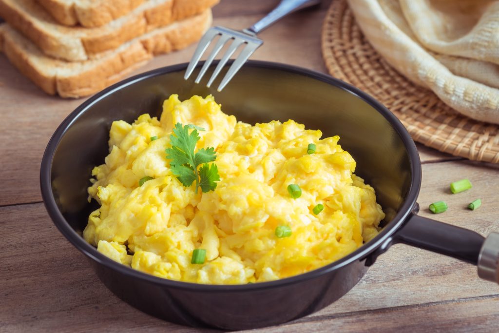 Scrambled egg in frying pan and toast on wooden table