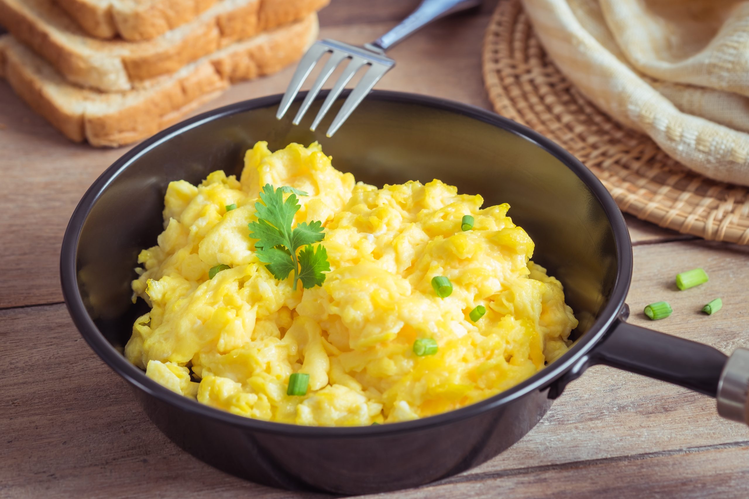 Scrambled egg in frying pan and toast on wooden table